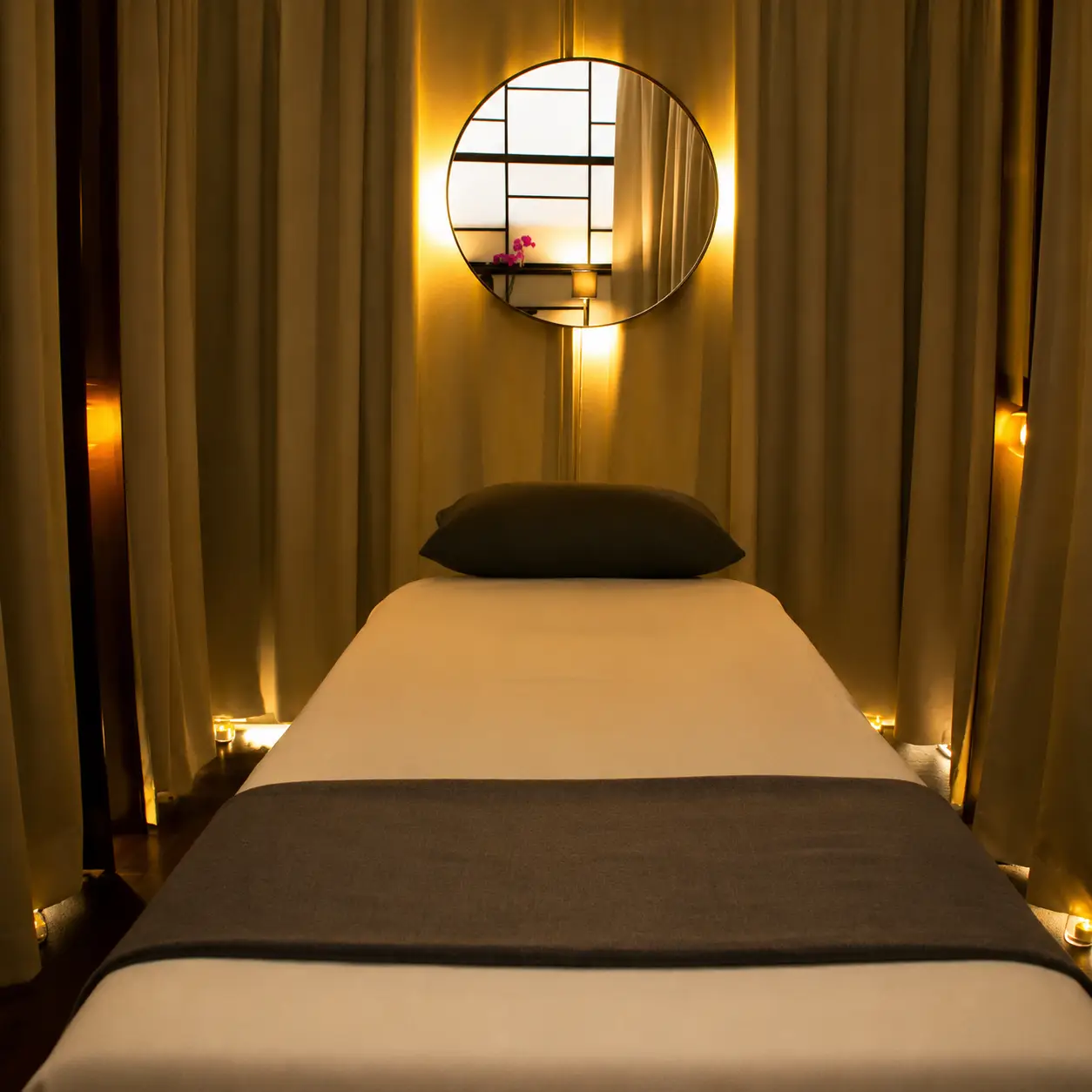 Sobre mí A clean massage table with white linens and a charcoal grey runner, prepared for a client in a softly lit spa room.